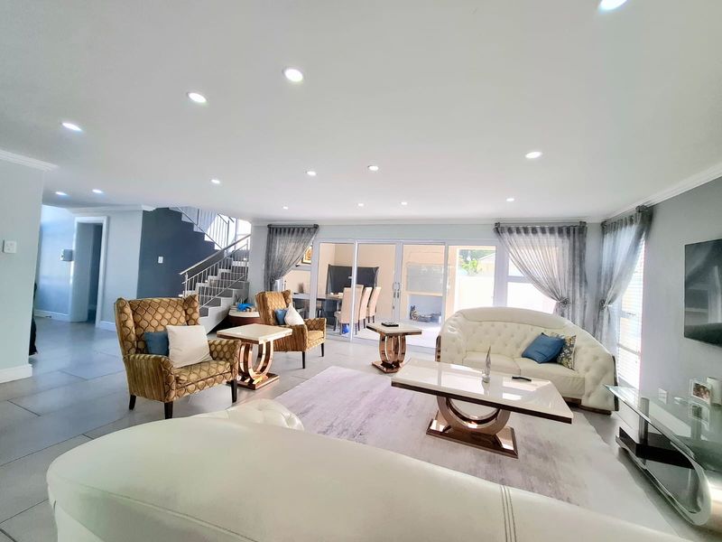 Spacious open-plan living area featuring modern tiled flooring, recessed downlighting, and a feature staircase, with large sliding doors providing access to the patio.