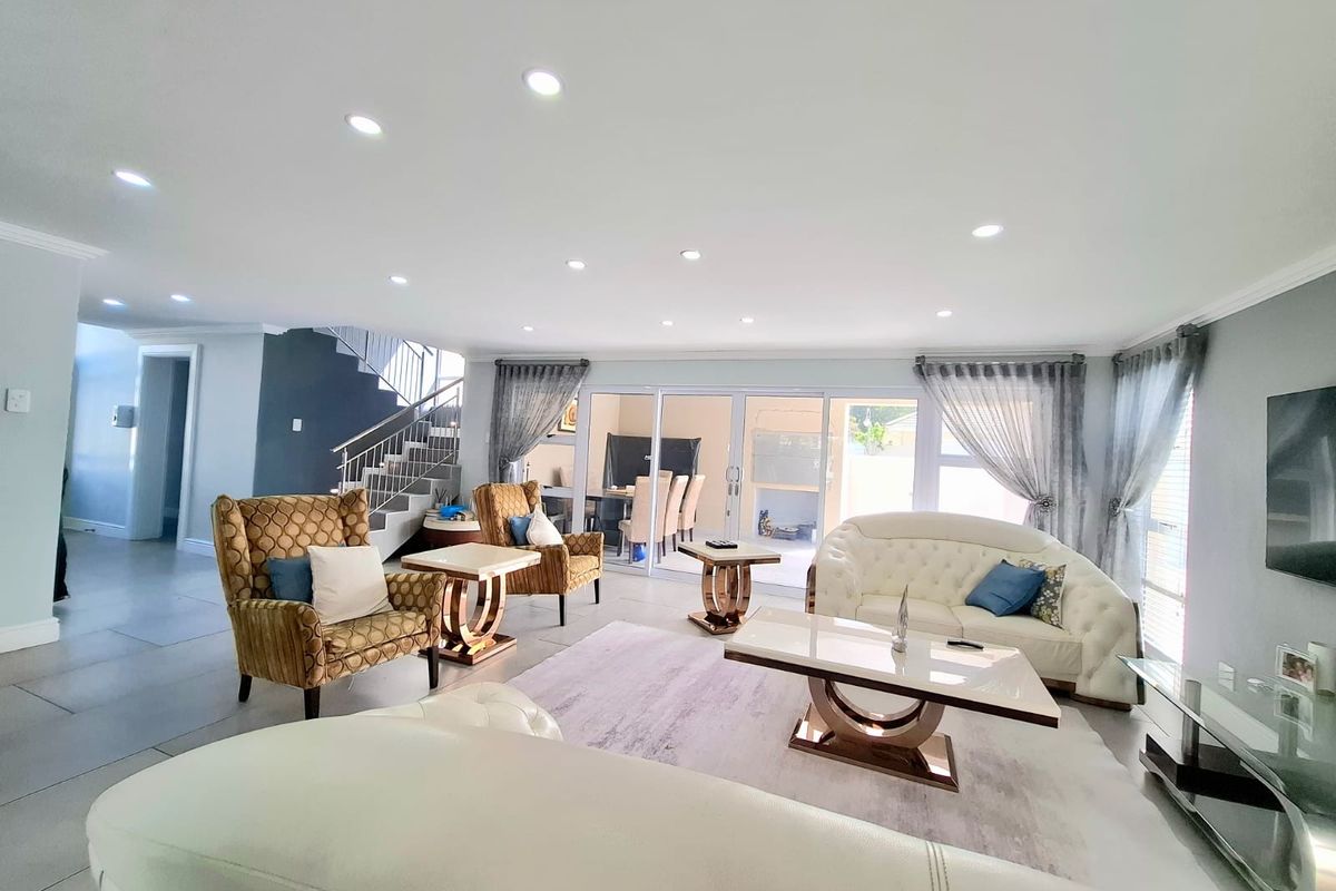 Spacious open-plan living area featuring modern tiled flooring, recessed downlighting, and a feature staircase, with large sliding doors providing access to the patio.