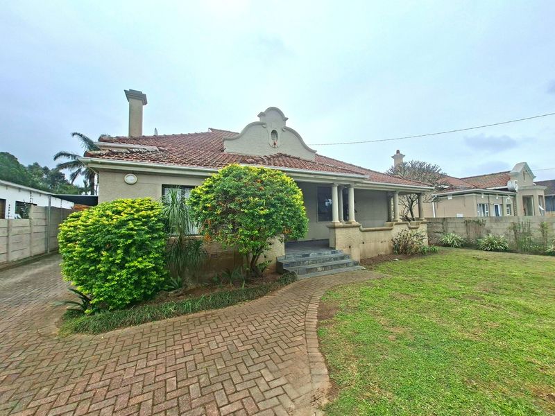 Front view of a single-story house featuring a tiled roof, covered porch, and a brick-paved driveway set within a landscaped garden.