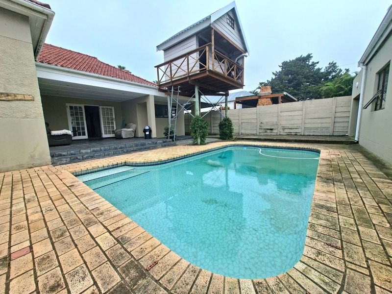 Outdoor pool area featuring a paved deck, covered patio access, and a raised wooden treehouse structure set within a private backyard.