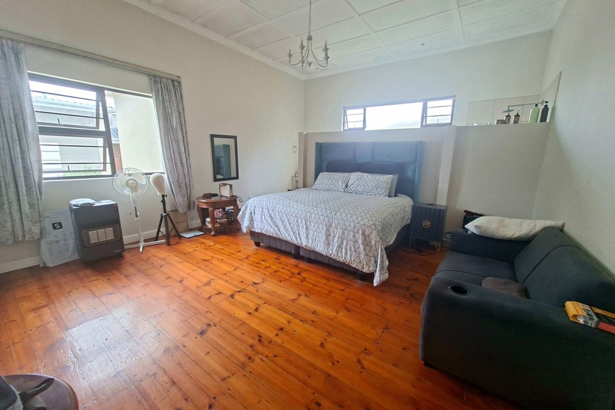 Spacious bedroom featuring original hardwood flooring, a high coffered ceiling, and a built-in headboard partition wall with integrated shelving.