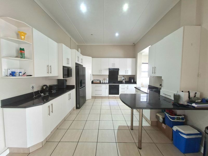 A spacious, modern kitchen featuring white cabinetry, dark granite countertops, built-in oven, extractor fan, and tiled flooring with ample workspace.