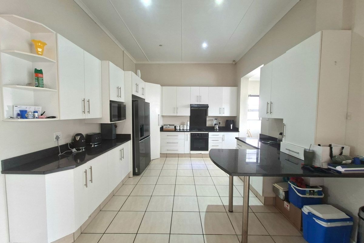A spacious, modern kitchen featuring white cabinetry, dark granite countertops, built-in oven, extractor fan, and tiled flooring with ample workspace.