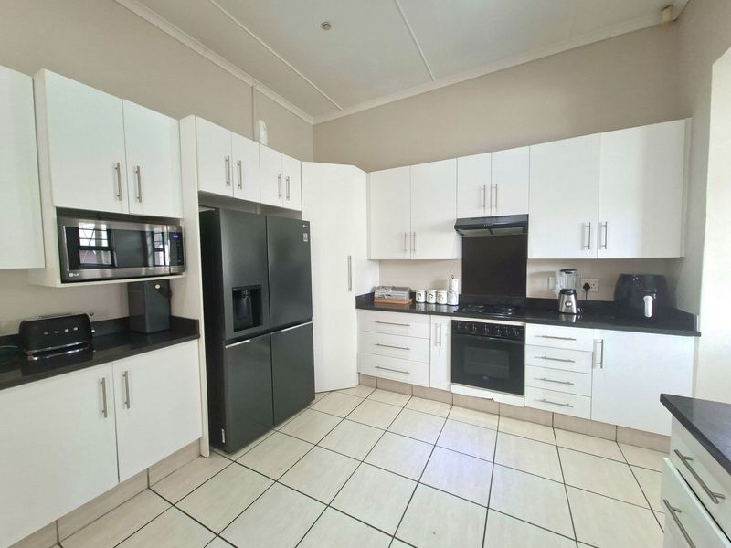 A well-maintained kitchen featuring white cabinetry, black granite countertops, built-in oven, gas hob, extractor fan, and tiled flooring.