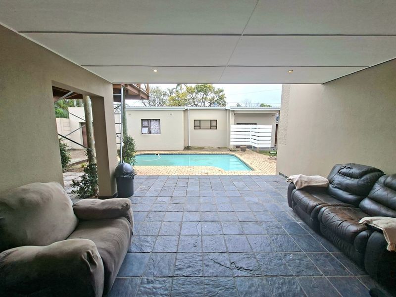 Covered outdoor patio area overlooking a swimming pool with paved surround and boundary walling.