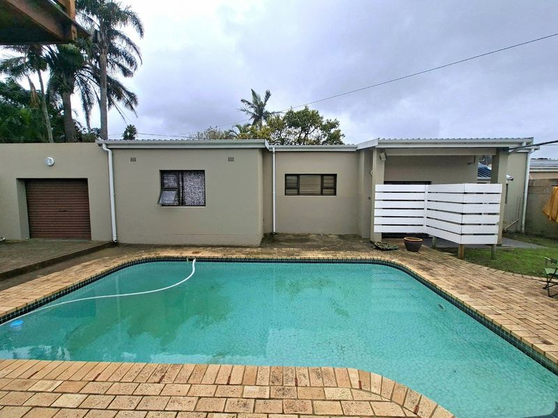 Rear exterior view featuring a swimming pool with brick coping, adjacent garage access, and a privacy screen against the main building structure.