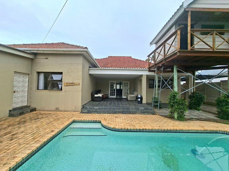 Rear exterior view featuring a swimming pool, paved surround, covered patio area, and an elevated wooden deck structure.