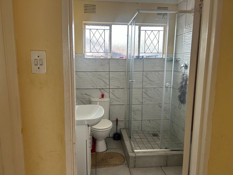 A functional bathroom featuring a glass shower enclosure, vanity basin, toilet, and tiled finishes, requiring minor cosmetic updates to refresh the space.