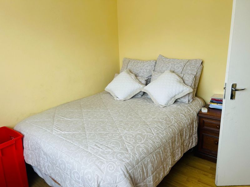 A compact bedroom featuring laminate flooring and yellow painted walls, providing a functional space for a single or double bed setup.