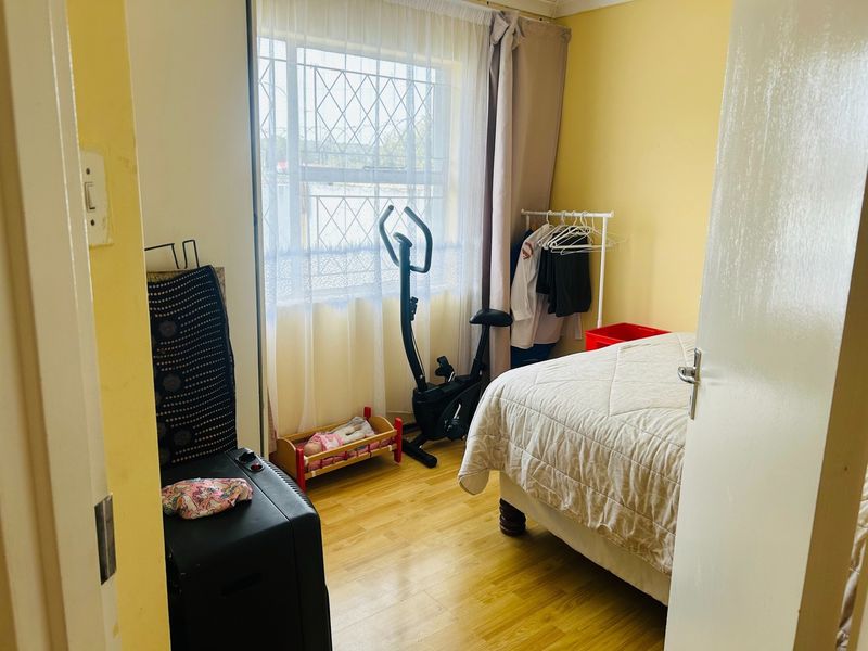 A standard bedroom featuring laminate flooring and a window with security bars, offering a functional space for rest.
