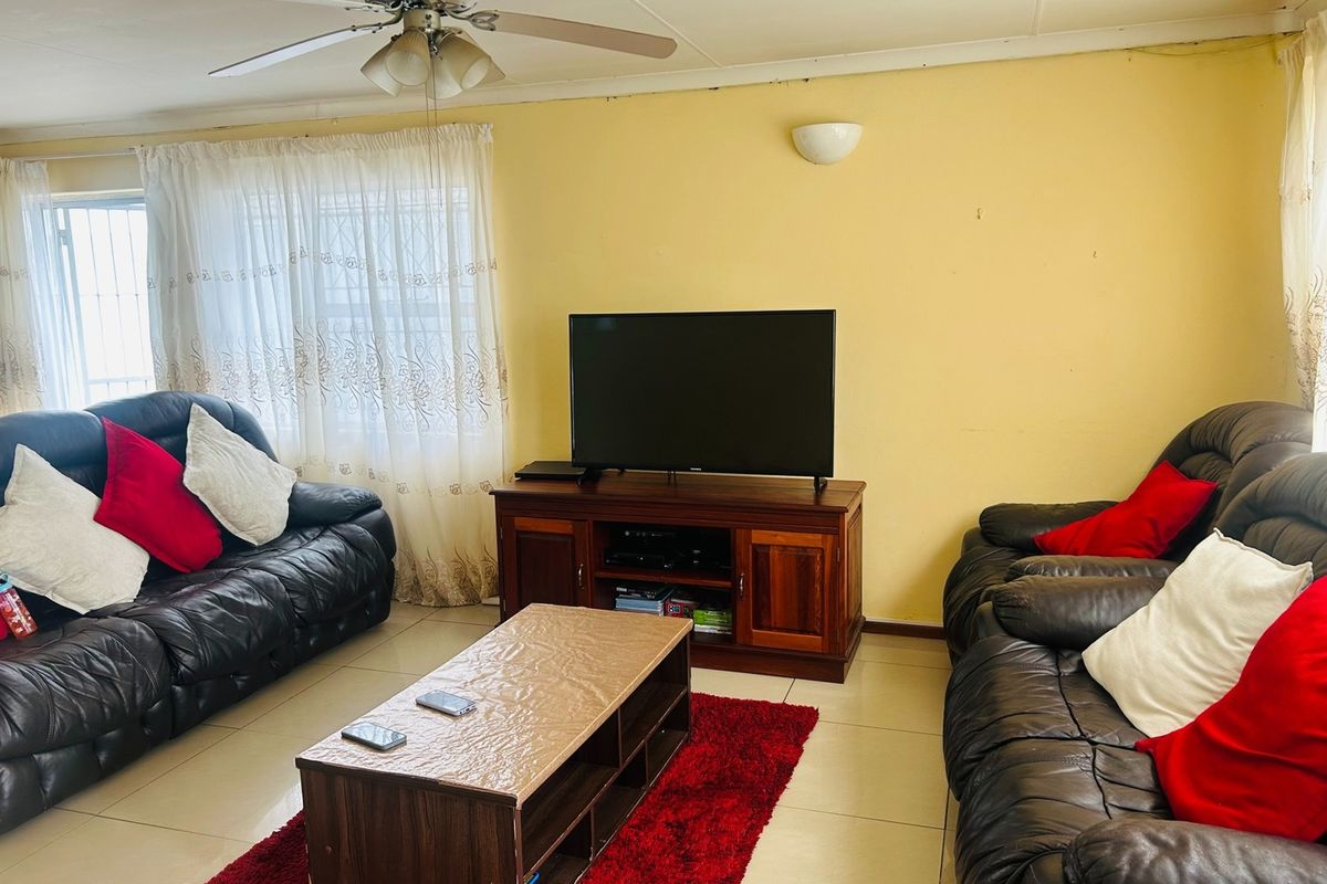 A living room featuring tiled flooring, a ceiling fan, and wall-mounted lighting, providing a functional space for relaxation.