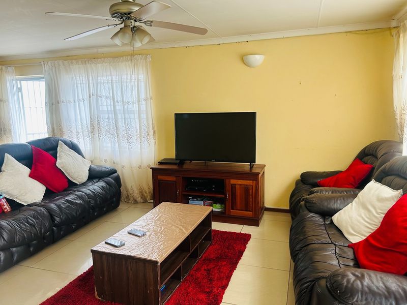 A living room featuring tiled flooring, a ceiling fan, and wall-mounted lighting, providing a functional space for relaxation.