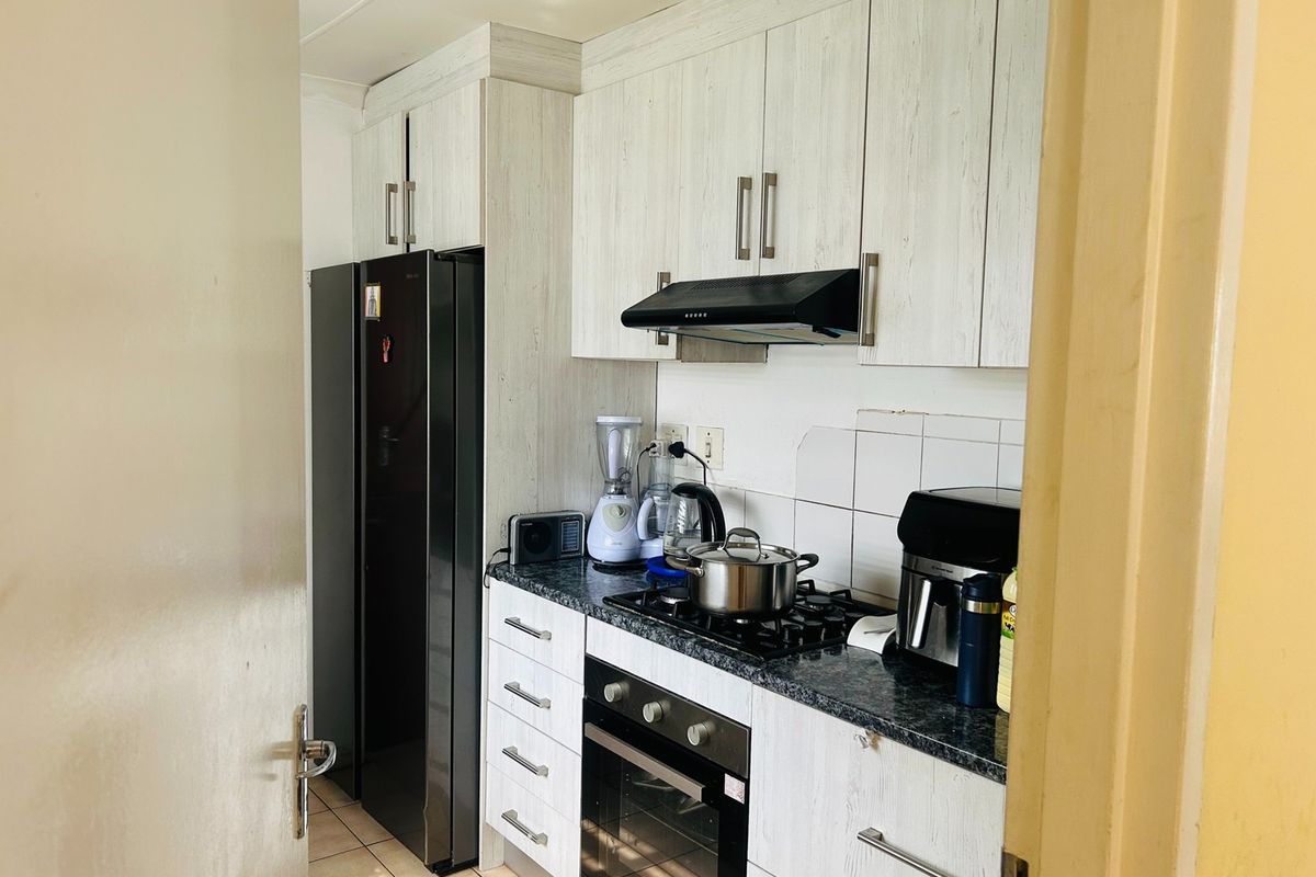 Compact kitchen featuring light wood-grain cabinetry, granite-look laminate countertops, a gas hob, built-in oven, and extractor fan.