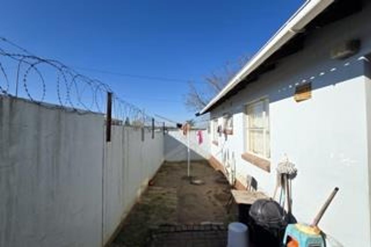 A narrow rear exterior area featuring a perimeter wall with razor wire and basic building facade.