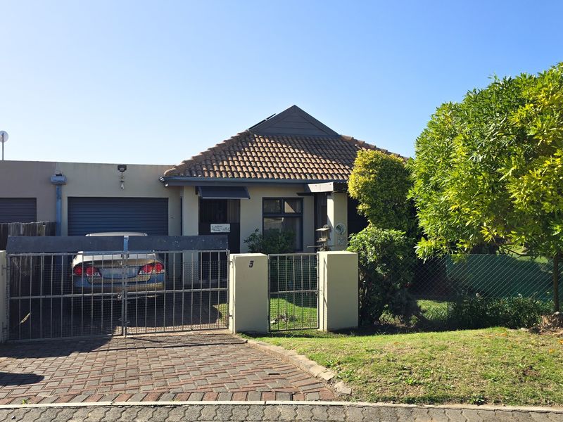 Front elevation of a townhouse featuring a tiled roof, paved driveway, and secure gated entrance with a garage.