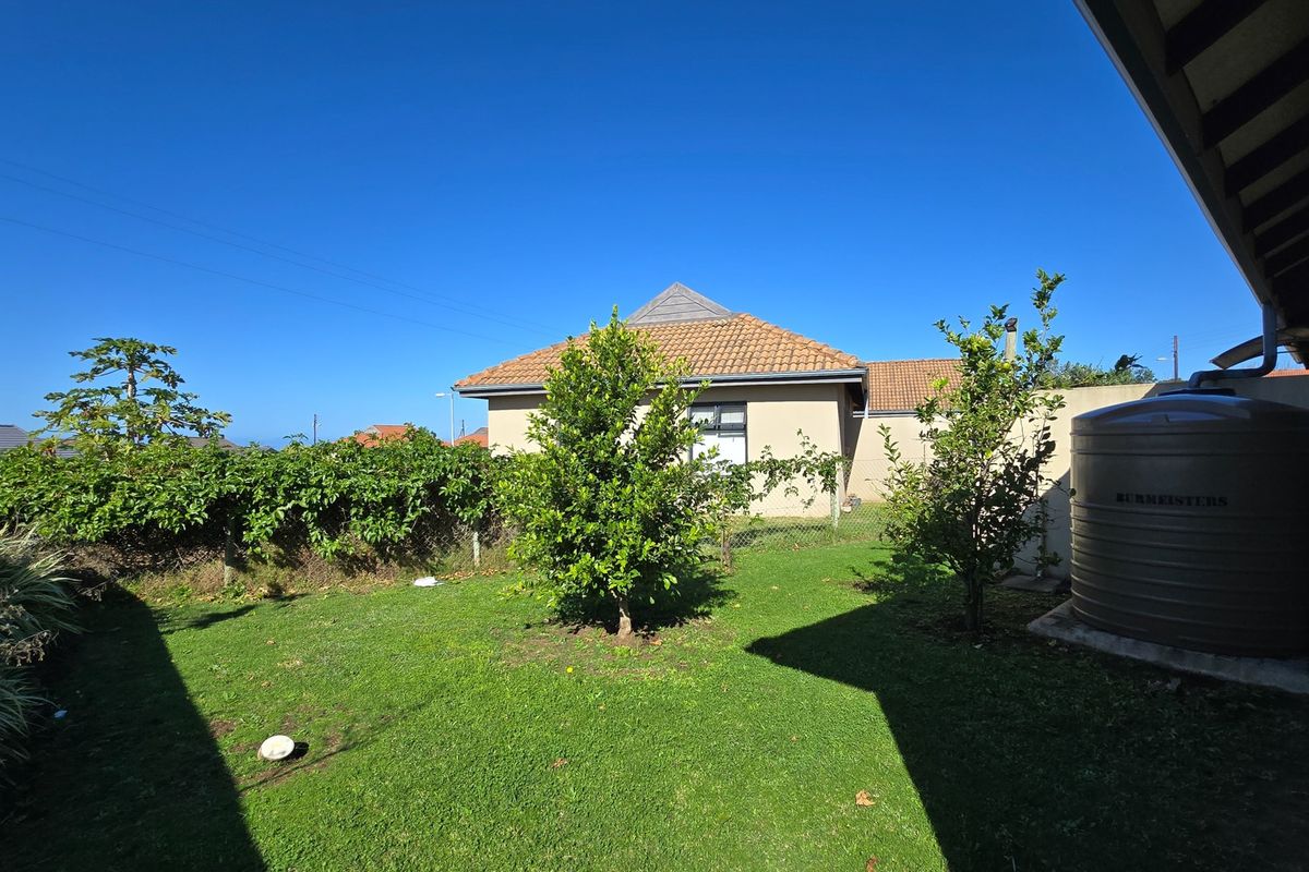 A private rear garden featuring a well-maintained lawn, established trees, and a large water storage tank attached to the property.