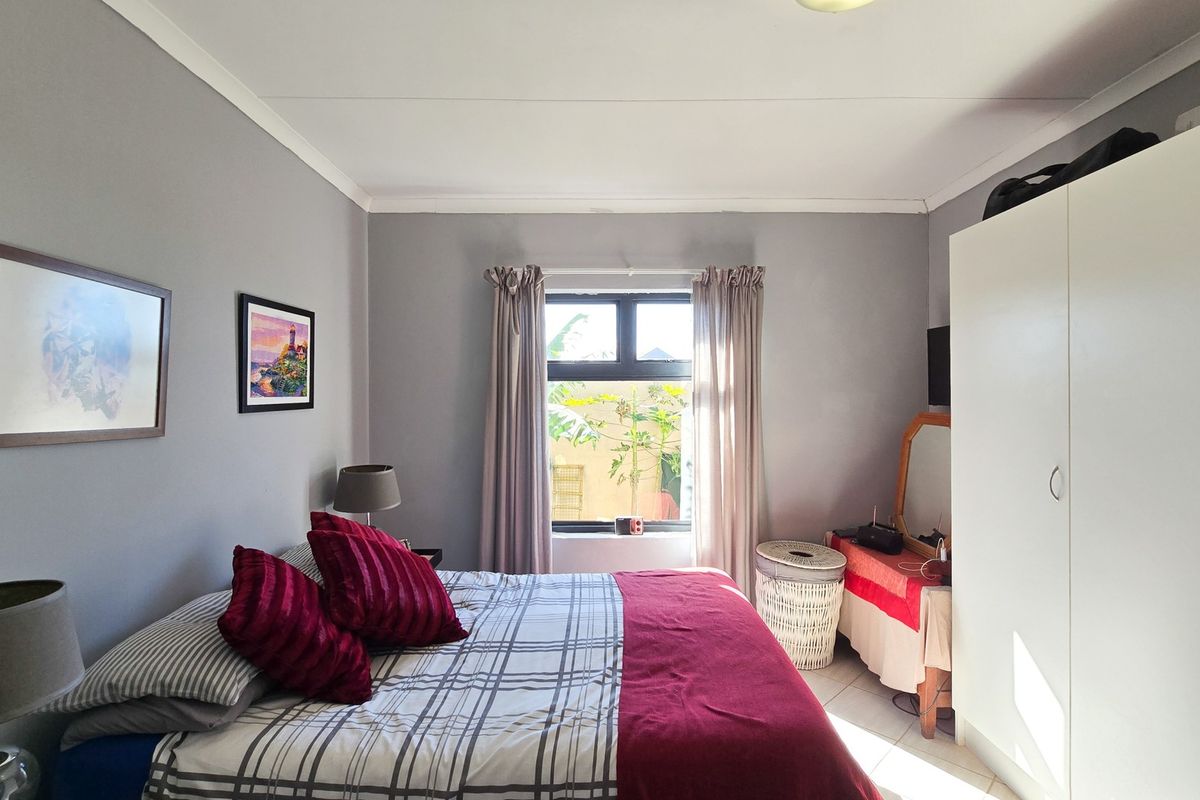 A well-lit bedroom featuring neutral grey walls, tiled flooring, a built-in wardrobe, and a window providing natural light.