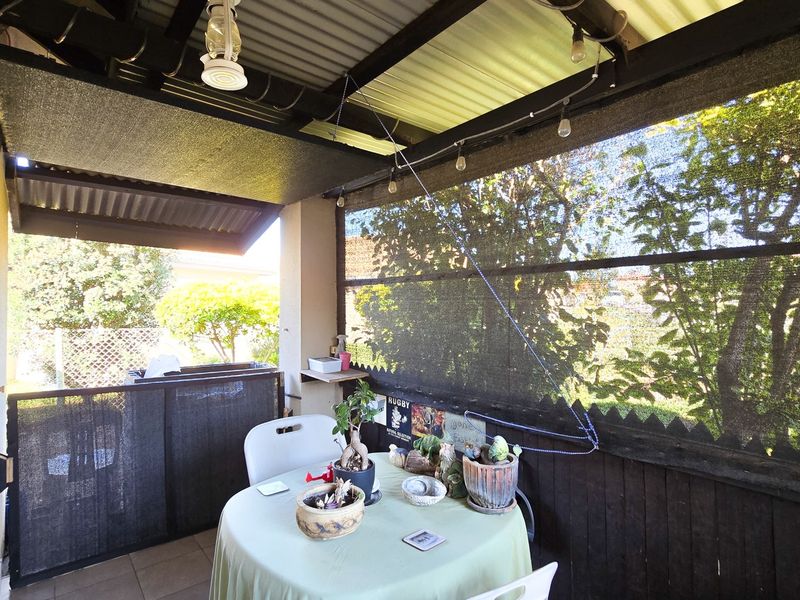 A covered patio area featuring tiled flooring, a corrugated roof, and privacy screening, providing a functional outdoor space for relaxation.
