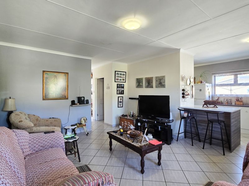 Open-plan living and kitchen area featuring tiled flooring, a central kitchen island with breakfast bar seating, and neutral wall finishes.