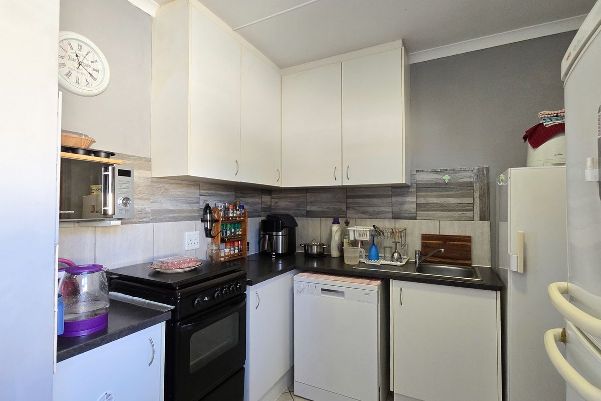 Compact kitchen featuring white cabinetry, dark laminate countertops, tiled backsplash, and integrated space for a dishwasher and freestanding stove.