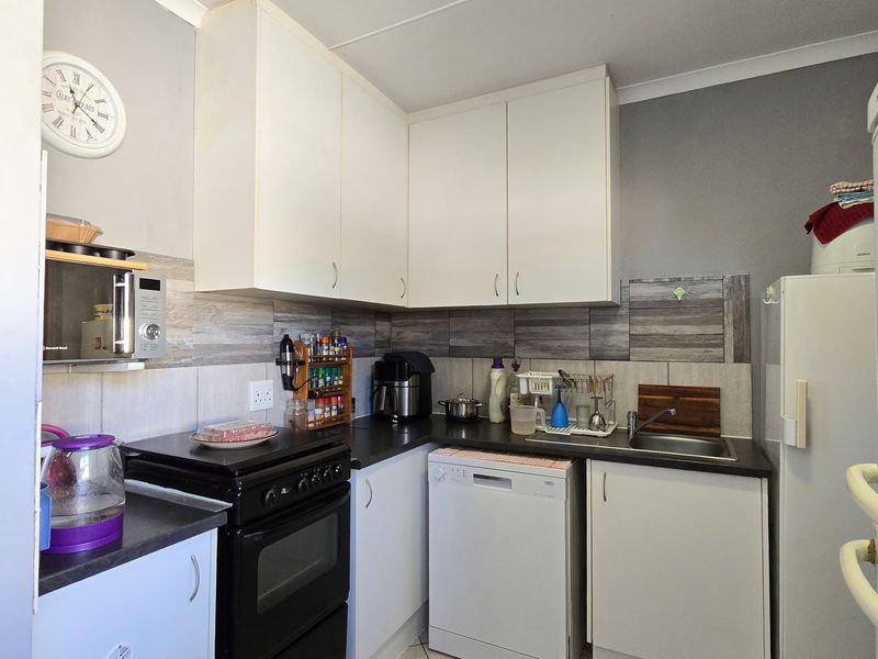 Compact kitchen featuring white cabinetry, dark laminate countertops, tiled backsplash, and integrated space for a dishwasher and freestanding stove.