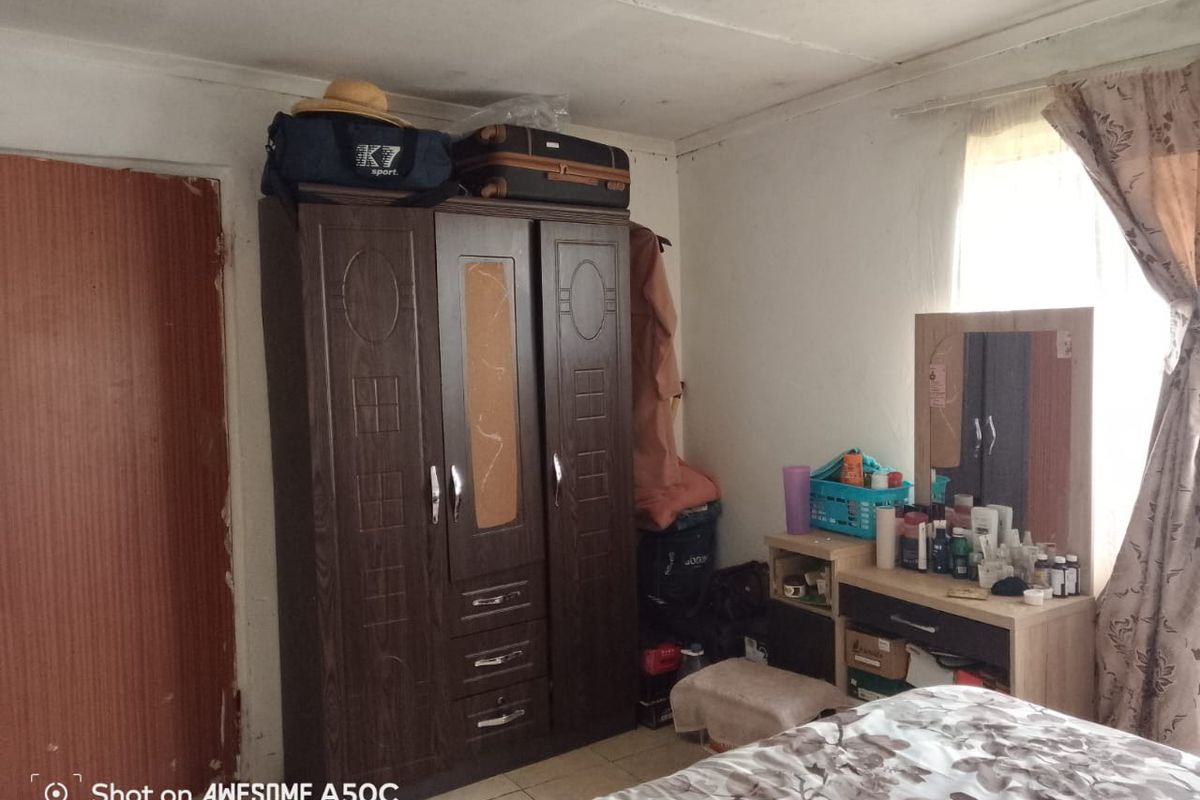 A bedroom featuring tiled flooring and a window, showing signs of ceiling water damage and general wear on the door frame.