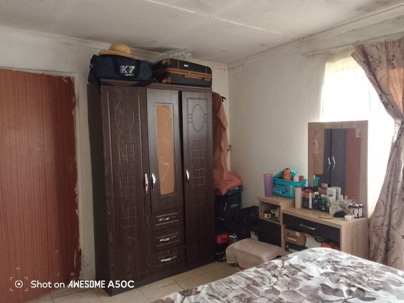 A bedroom featuring tiled flooring and a window, showing signs of ceiling water damage and general wear on the door frame.