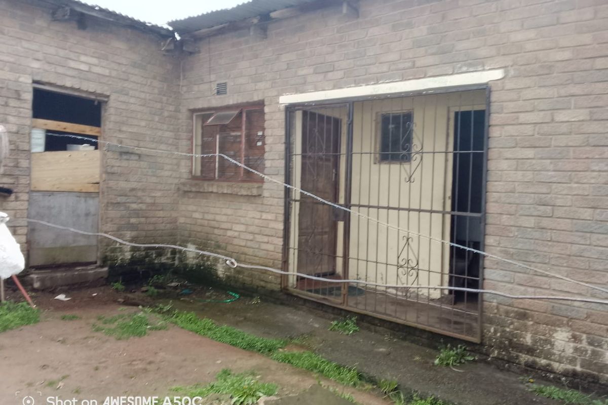 Rear exterior view of a brick house featuring security gates and bars, showing signs of significant wear and maintenance requirements.