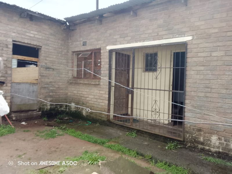 Rear exterior view of a brick house featuring security gates and bars, showing signs of significant wear and maintenance requirements.