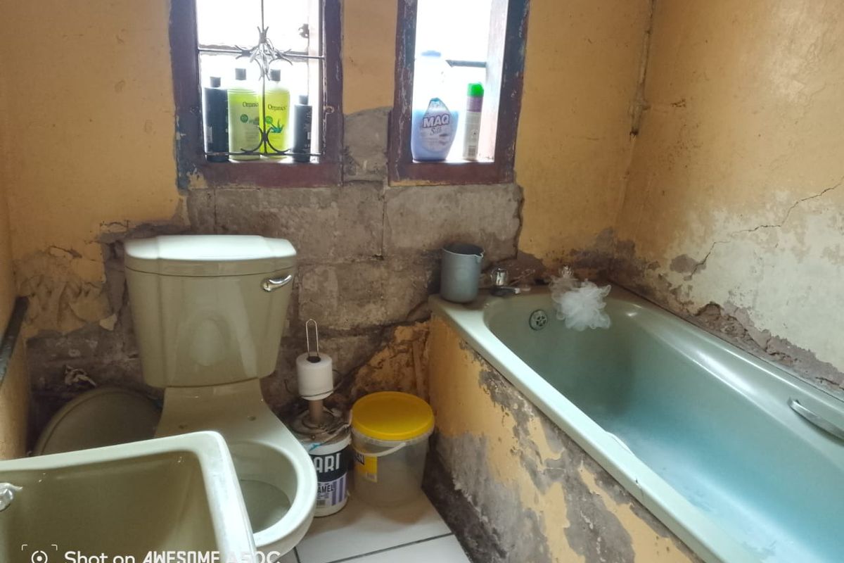 A bathroom in need of significant renovation, featuring a toilet, bathtub, and basin with visible wall damage and exposed masonry.