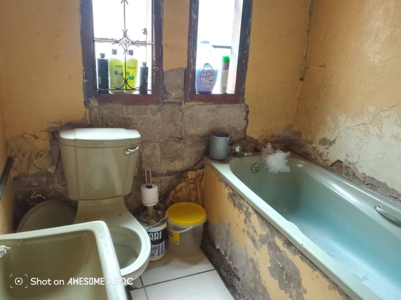 A bathroom in need of significant renovation, featuring a toilet, bathtub, and basin with visible wall damage and exposed masonry.