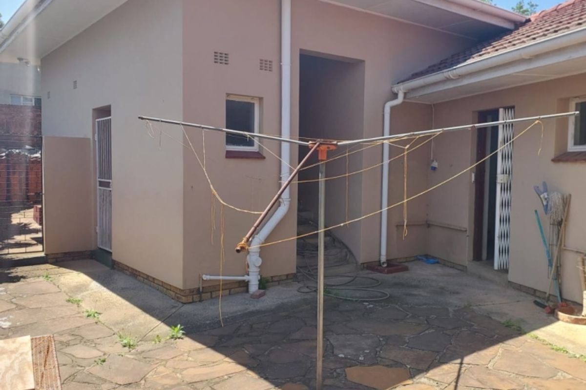 Rear exterior view of the property featuring a paved patio area, security gates, and external drainage infrastructure.