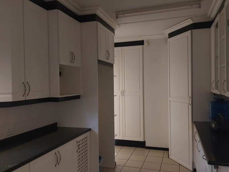 A functional scullery or utility area featuring ample built-in white cabinetry, dark countertops, and tiled flooring, providing practical storage and workspace.