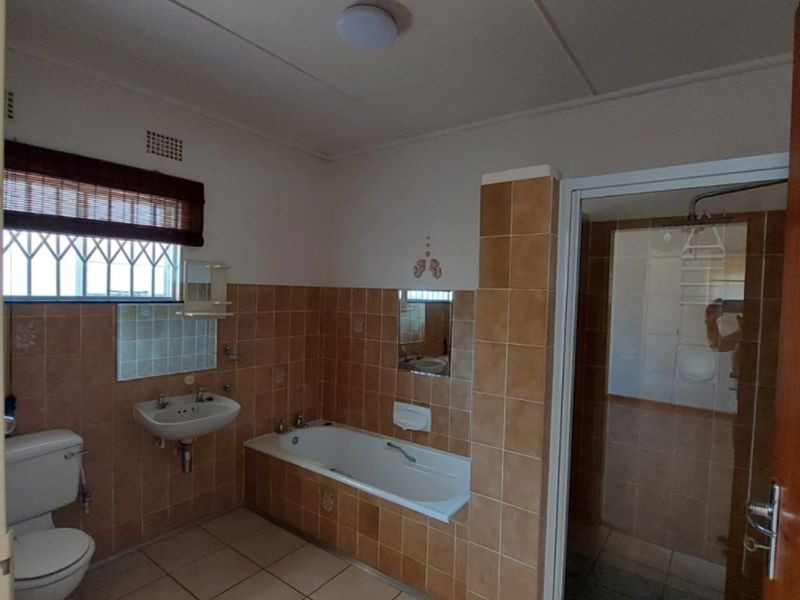 A functional bathroom featuring a built-in bathtub, separate shower enclosure, wall-mounted basin, and tiled finishes throughout.