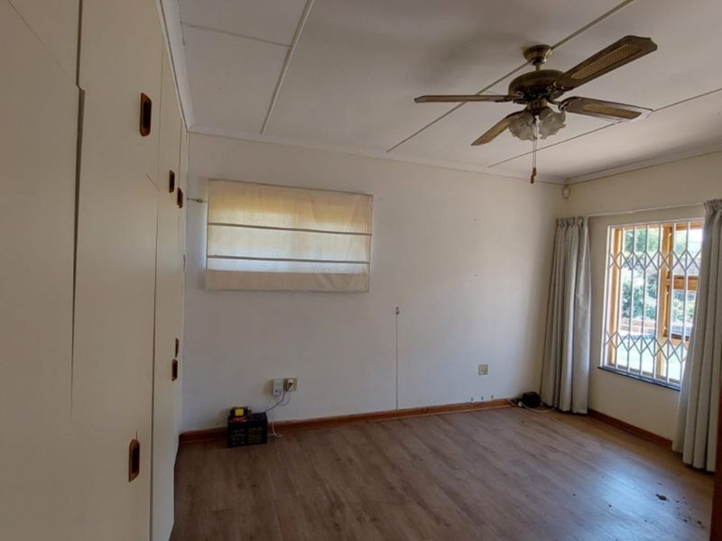 A vacant bedroom featuring built-in cupboards, a ceiling fan, and laminate flooring, with security bars installed on the window.