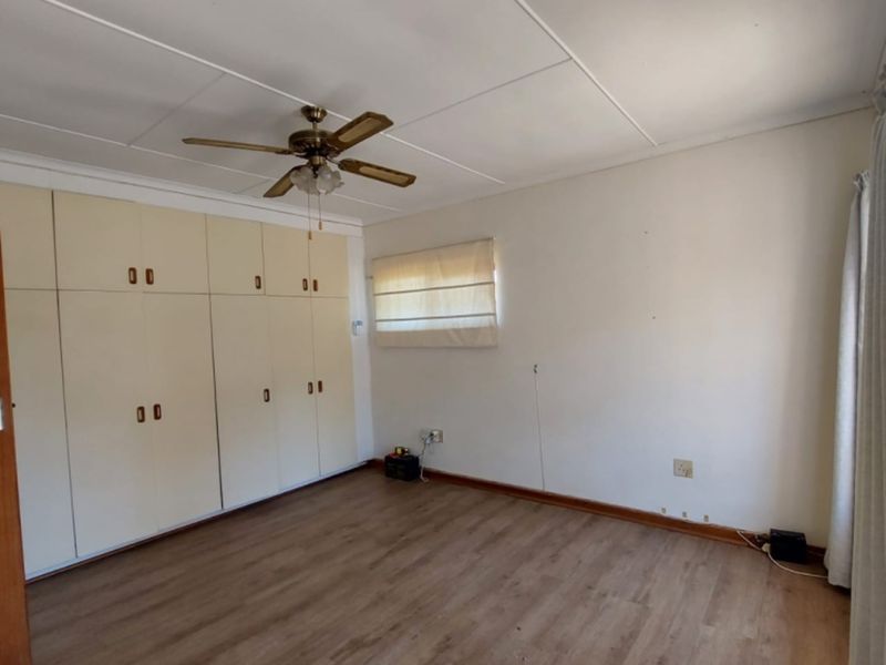 A spacious, empty bedroom featuring laminate flooring, a ceiling fan, and extensive built-in cupboard storage.