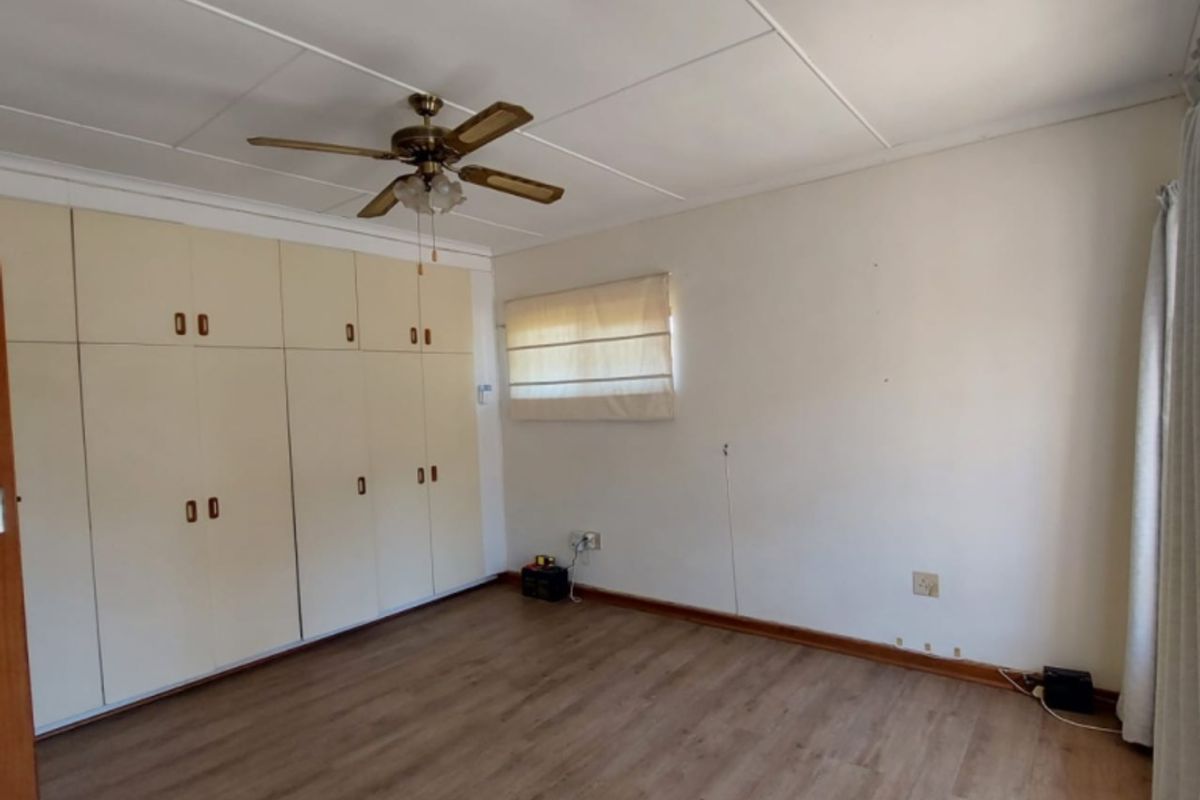 A spacious, empty bedroom featuring laminate flooring, a ceiling fan, and extensive built-in cupboard storage.