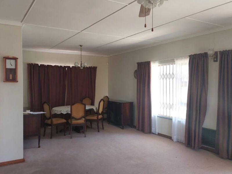 Spacious living area featuring a ceiling fan, security gate on windows, and carpeted flooring, offering a functional space with potential for modernization.