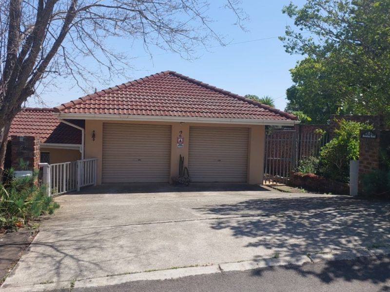 Front view of a residential property featuring a double garage with roll-up doors, a concrete driveway, and established boundary walling.