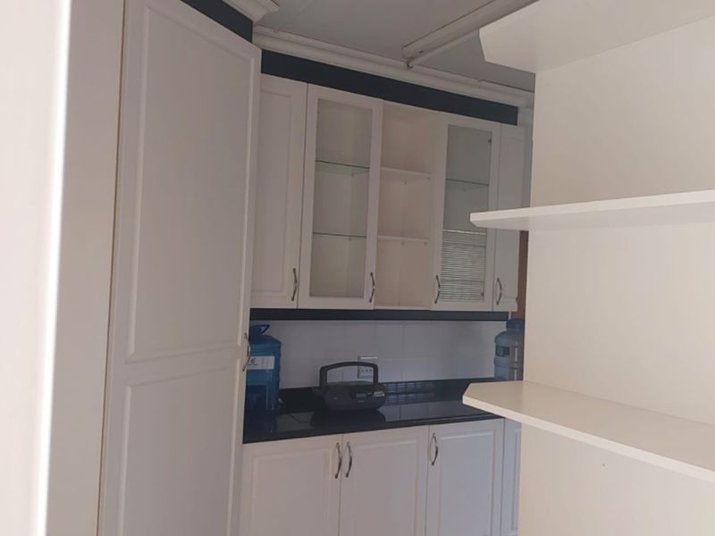 A clean and functional scullery area featuring white built-in cabinetry, dark stone countertops, and convenient open shelving for additional storage.