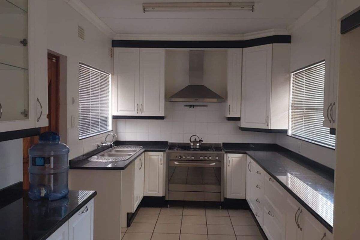 A functional kitchen featuring white cabinetry, contrasting black granite countertops, stainless steel gas stove, extractor fan, and tiled flooring.