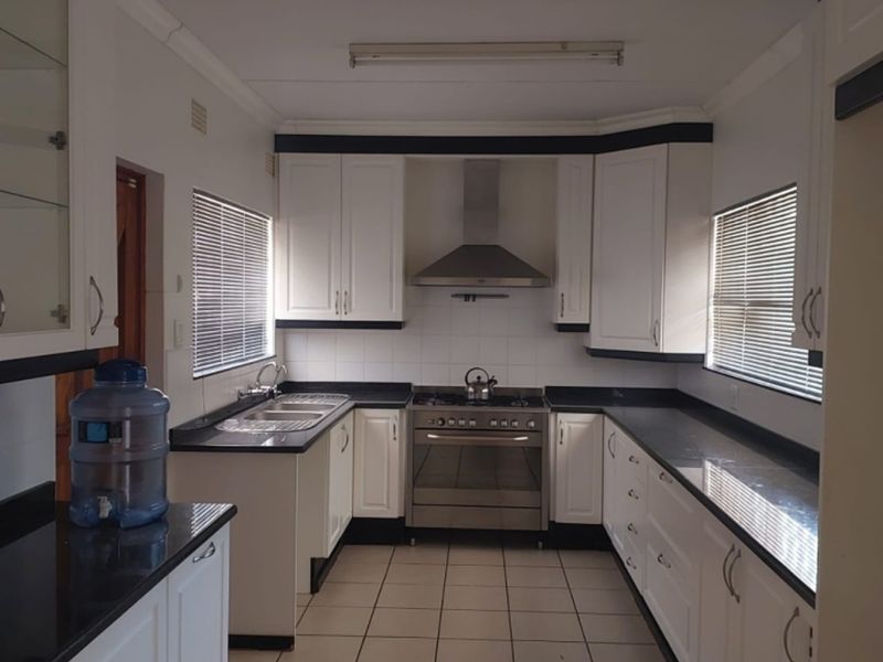 A functional kitchen featuring white cabinetry, contrasting black granite countertops, stainless steel gas stove, extractor fan, and tiled flooring.