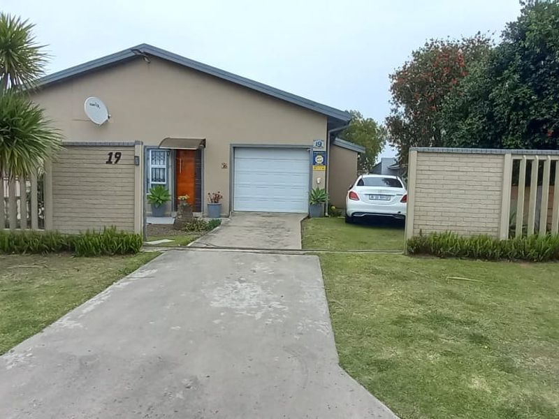 Front elevation of a single-story house featuring a concrete driveway, a sectional garage door, and a brick boundary wall with a gated entrance.