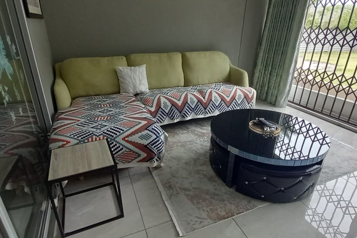 A living room area featuring tiled flooring and a large sliding glass door with an integrated security gate, providing access to the outdoor space.