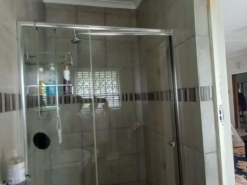 A bathroom featuring a tiled shower enclosure with a glass door, adjacent to a bedroom area with built-in wooden cabinetry.