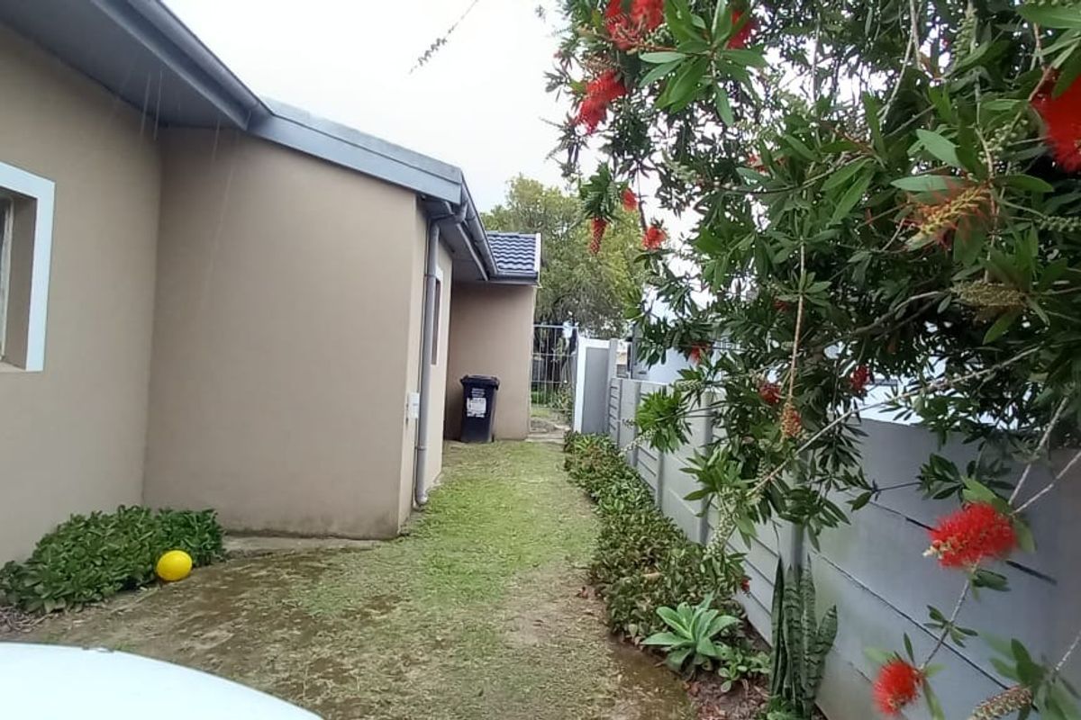 A view of the rear exterior area featuring a side pathway, precast boundary wall, and established garden greenery.