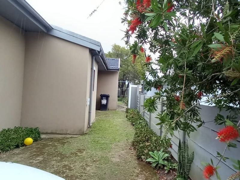 A view of the rear exterior area featuring a side pathway, precast boundary wall, and established garden greenery.