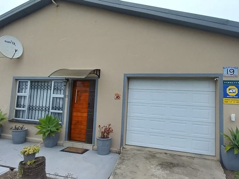 Front elevation of the property featuring a single garage, secure entrance door with awning, and paved driveway area.