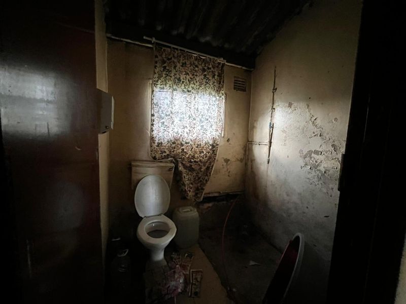 A small, dated bathroom requiring significant renovation, featuring a standard toilet and visible wall surface deterioration.