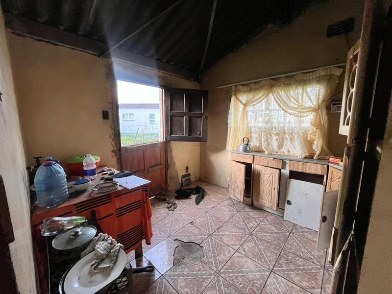 A kitchen space requiring significant renovation, featuring damaged floor tiles, worn cabinetry, and an exposed roof structure.